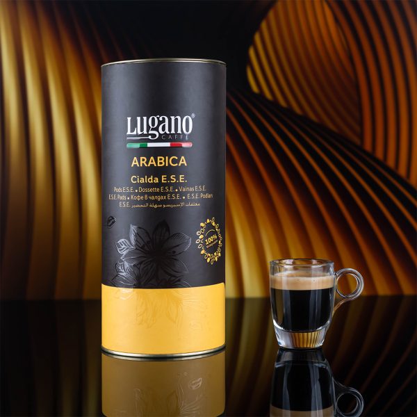 Lugano Caffè Arabica Espresso Pod 18 pcs cylinder pack and a cup in a studio set